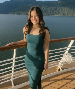 A woman in a green dress smiling in front of a body of water. 